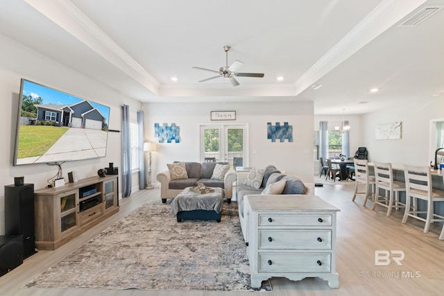 living room with crown molding, ceiling fan with notable chandelier, light wood-type flooring, and a tray ceiling