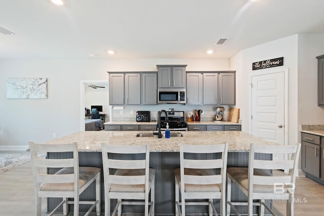 kitchen with a kitchen island with sink, gray cabinets, light hardwood / wood-style floors, appliances with stainless steel finishes, and sink