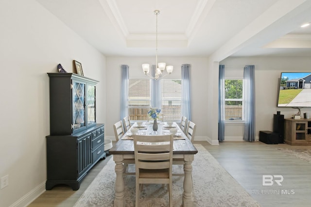 dining space with a notable chandelier, crown molding, light wood-type flooring, and a tray ceiling