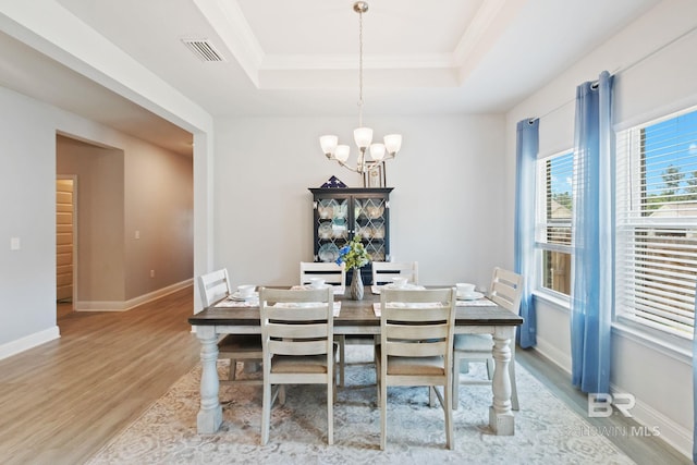 dining room with crown molding, a chandelier, light wood-type flooring, and a tray ceiling