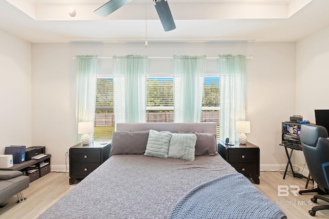 bedroom with a raised ceiling, ceiling fan, and light wood-type flooring