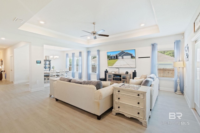 living room featuring light wood-type flooring, ceiling fan with notable chandelier, and a raised ceiling