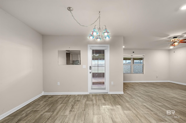 spare room featuring ceiling fan with notable chandelier, wood finished floors, and baseboards