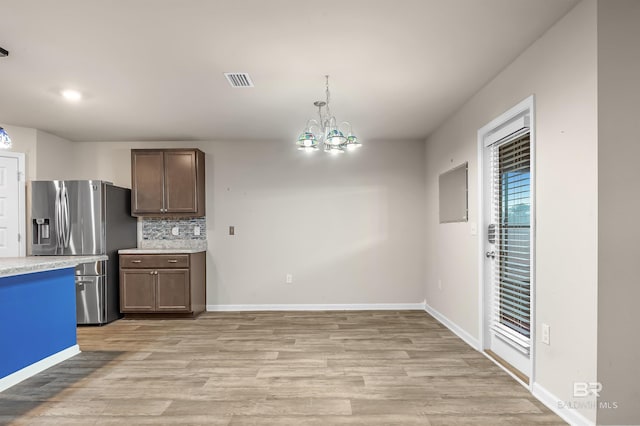 kitchen featuring a notable chandelier, stainless steel fridge, light wood finished floors, decorative backsplash, and light countertops