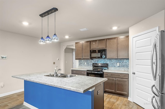 kitchen with tasteful backsplash, light wood-type flooring, light countertops, black appliances, and a sink