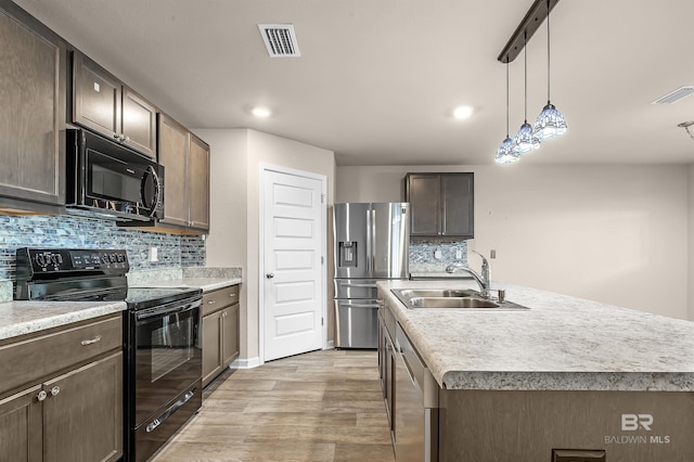 kitchen featuring visible vents, black appliances, light wood-style floors, and a sink