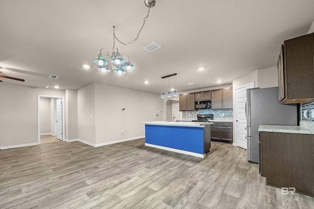 kitchen with visible vents, a center island with sink, stainless steel appliances, light countertops, and decorative backsplash