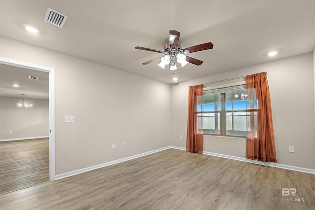 spare room with ceiling fan with notable chandelier, wood finished floors, visible vents, and baseboards