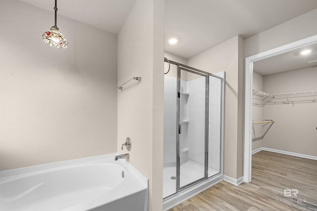 bathroom featuring a walk in closet, a stall shower, wood finished floors, baseboards, and a bath