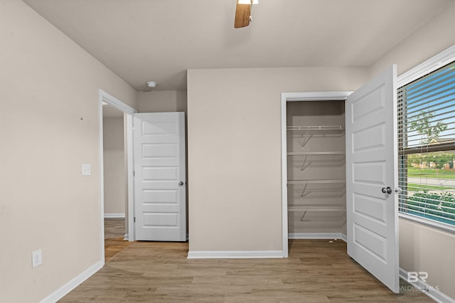 unfurnished bedroom featuring a closet, baseboards, a walk in closet, and light wood-style floors