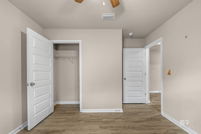 unfurnished bedroom featuring wood finished floors, visible vents, a closet, and baseboards