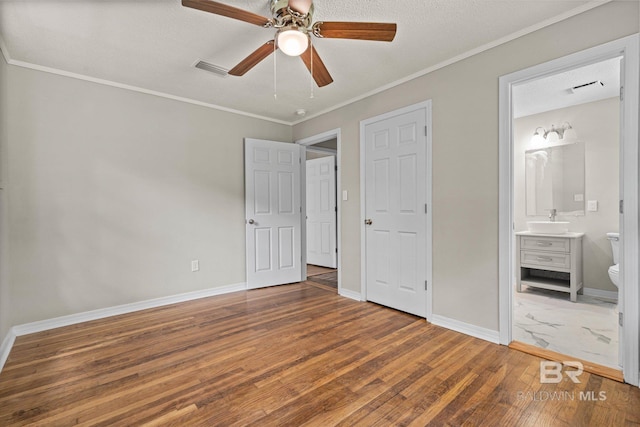 unfurnished bedroom with hardwood / wood-style floors, visible vents, ornamental molding, a sink, and baseboards