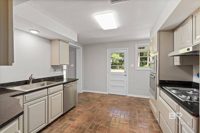 kitchen featuring under cabinet range hood, a sink, brick floor, baseboards, and appliances with stainless steel finishes