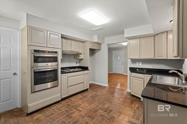 kitchen with black electric cooktop, a sink, baseboards, under cabinet range hood, and double oven