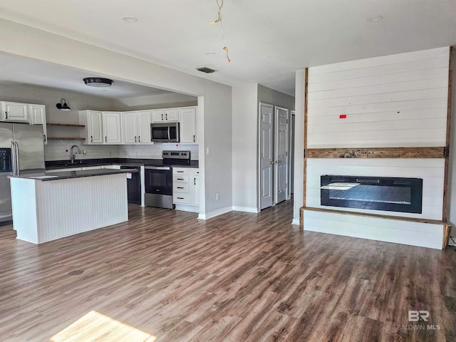 kitchen featuring hardwood / wood-style flooring, stainless steel appliances, tasteful backsplash, a large fireplace, and white cabinets