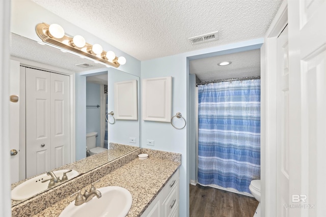 bathroom with toilet, vanity, a textured ceiling, and hardwood / wood-style floors