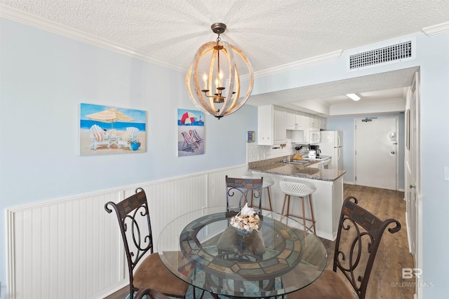 dining space featuring a textured ceiling, an inviting chandelier, hardwood / wood-style floors, and crown molding