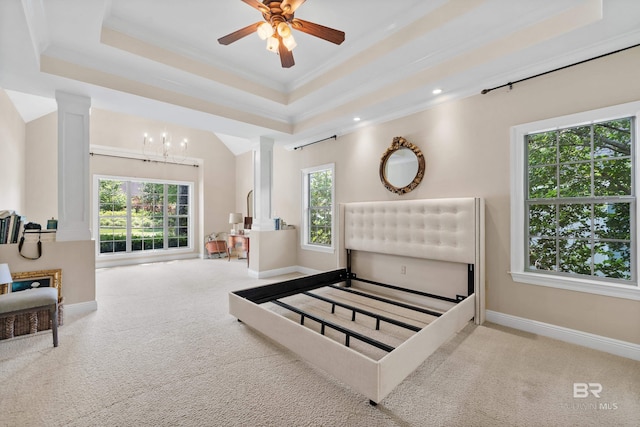 bedroom featuring a tray ceiling, multiple windows, and ornate columns