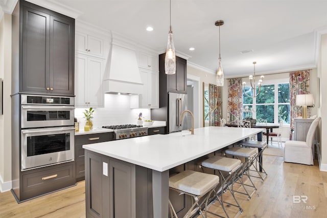 kitchen with appliances with stainless steel finishes, light wood-type flooring, custom exhaust hood, a center island with sink, and a breakfast bar area