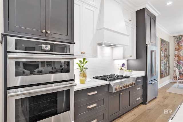 kitchen featuring white cabinets, crown molding, light hardwood / wood-style floors, custom range hood, and stainless steel appliances