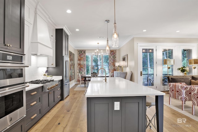 kitchen featuring pendant lighting, custom exhaust hood, an island with sink, light hardwood / wood-style floors, and stainless steel appliances