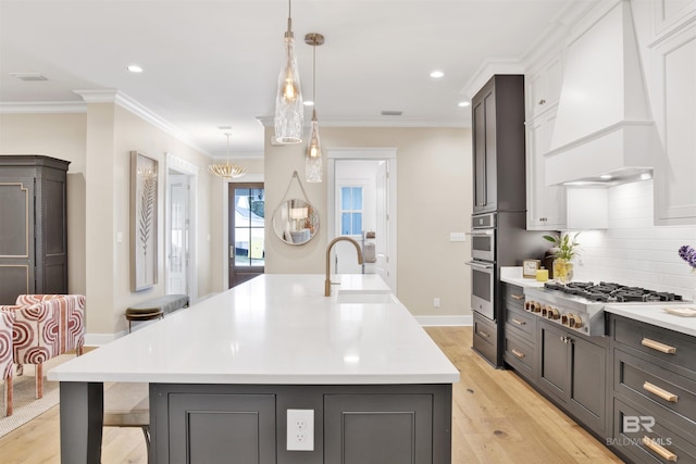 kitchen with custom exhaust hood, light hardwood / wood-style flooring, stainless steel appliances, and an island with sink