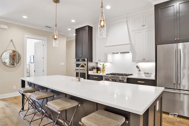 kitchen with appliances with stainless steel finishes, light wood-type flooring, an island with sink, and custom exhaust hood