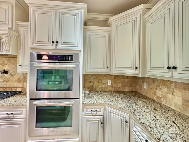 kitchen with double oven, cream cabinets, ornamental molding, light stone counters, and tasteful backsplash