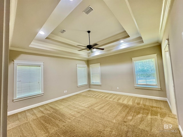 empty room with crown molding, a tray ceiling, light colored carpet, and ceiling fan