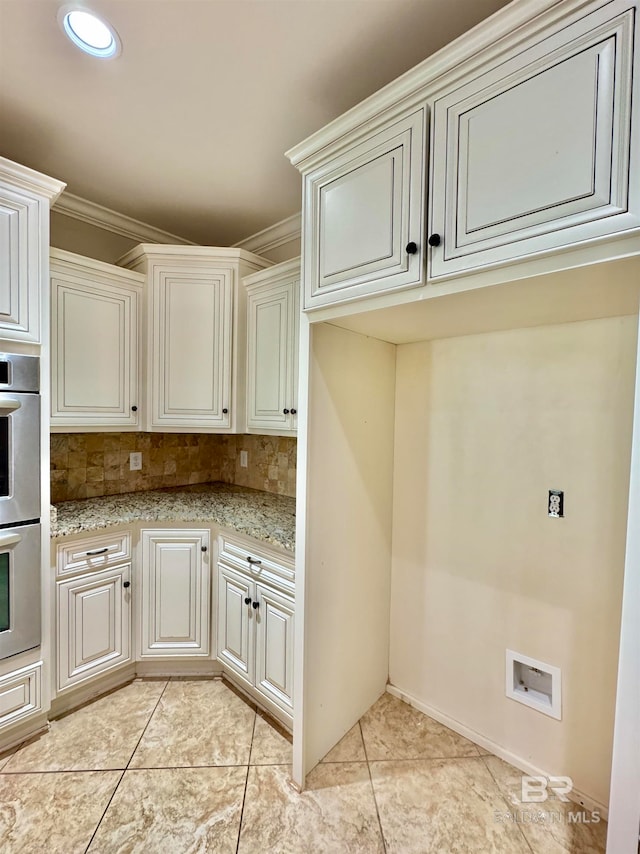 kitchen featuring decorative backsplash, stainless steel double oven, ornamental molding, light tile patterned flooring, and light stone counters