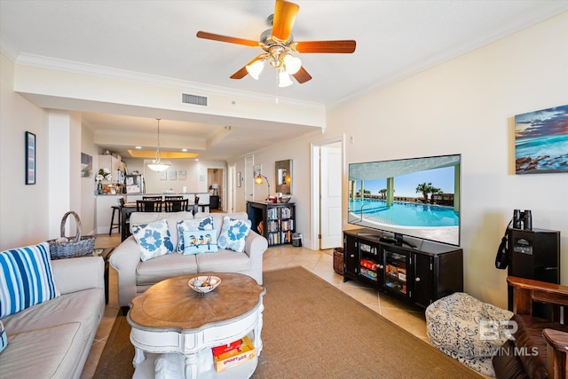 living area featuring light tile patterned floors, visible vents, a ceiling fan, a raised ceiling, and crown molding