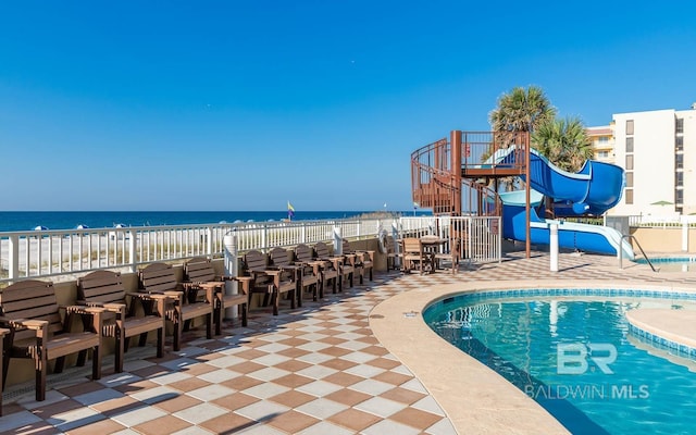 view of swimming pool featuring a patio area, a water slide, a water view, and fence