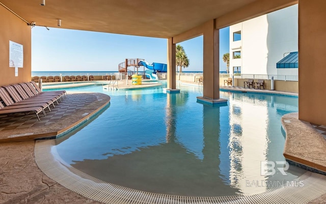 pool with a water view, a hot tub, a water slide, and a patio