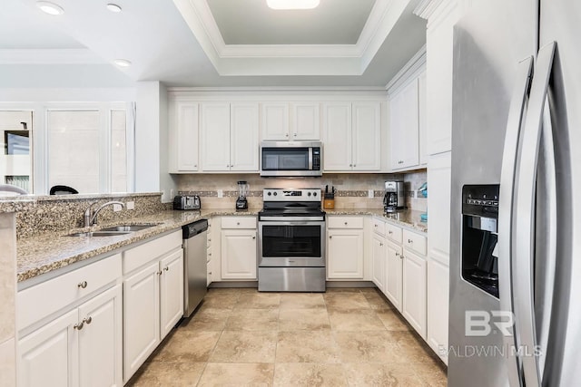 kitchen featuring a raised ceiling, appliances with stainless steel finishes, white cabinetry, a sink, and light stone countertops