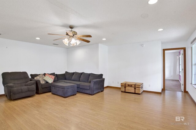 living room featuring light wood-type flooring, ceiling fan, and a textured ceiling