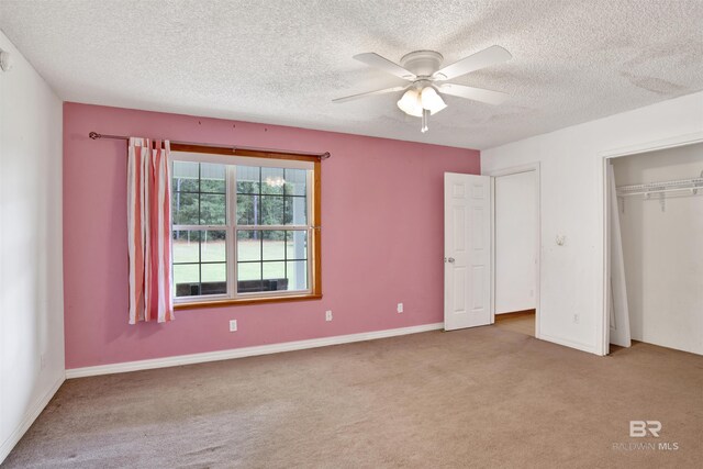 unfurnished bedroom with a textured ceiling, light colored carpet, ceiling fan, and a closet