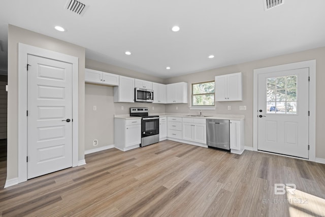 kitchen featuring light wood finished floors, white cabinets, appliances with stainless steel finishes, light countertops, and a sink