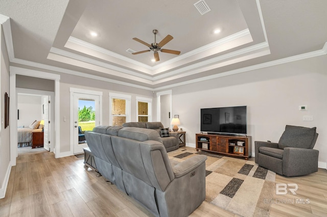 living room with a raised ceiling, light wood-style floors, a ceiling fan, baseboards, and visible vents