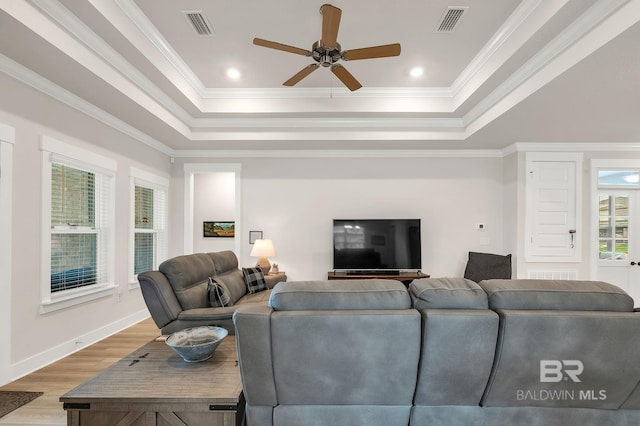 living room with a ceiling fan, visible vents, a raised ceiling, and light wood-type flooring
