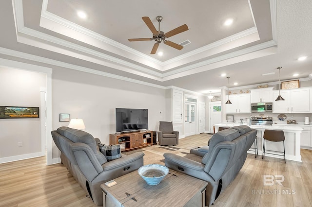 living area featuring crown molding, ceiling fan, a tray ceiling, and light wood-type flooring