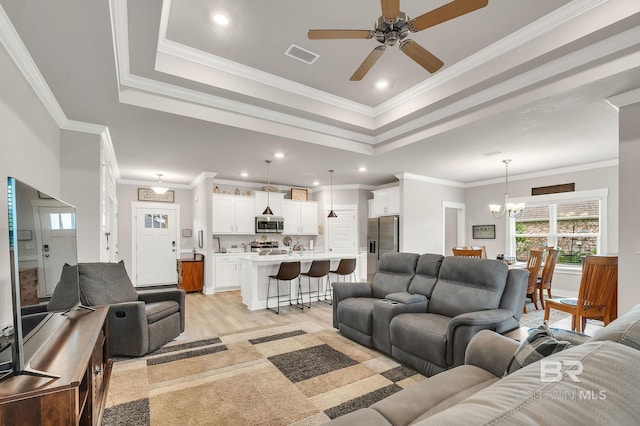 living area with a tray ceiling, visible vents, ornamental molding, and ceiling fan with notable chandelier