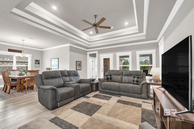 living room with crown molding, a raised ceiling, ceiling fan with notable chandelier, and light wood finished floors