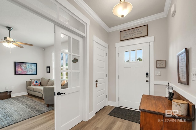 foyer entrance featuring crown molding, a ceiling fan, baseboards, and light wood-type flooring
