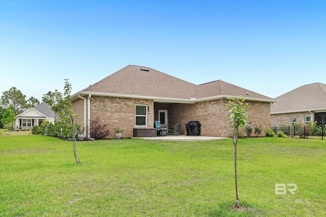 back of house featuring fence, a shingled roof, brick siding, a lawn, and a patio