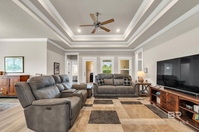 living room featuring light wood-type flooring, a ceiling fan, a tray ceiling, and ornamental molding
