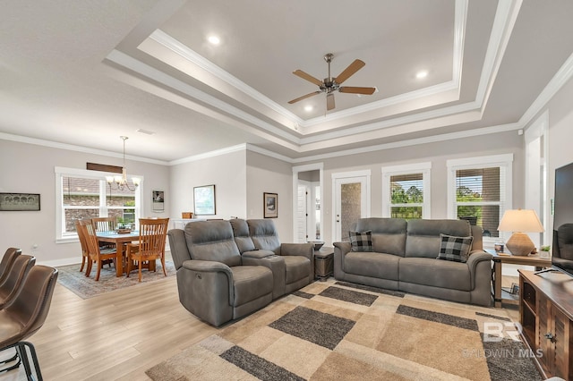 living area with plenty of natural light, light wood-style flooring, ceiling fan with notable chandelier, and a tray ceiling