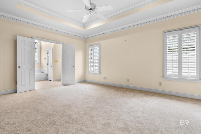 unfurnished bedroom with ceiling fan, a tray ceiling, light carpet, crown molding, and ensuite bathroom