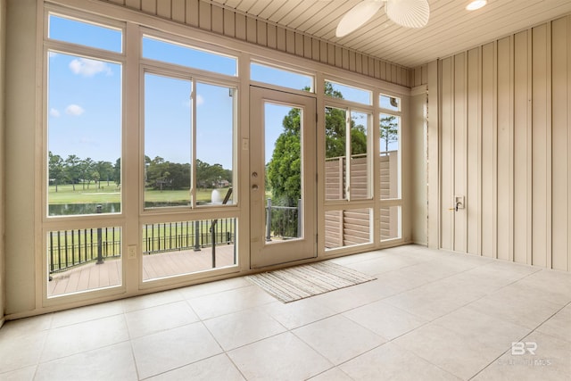 doorway featuring wood ceiling, wooden walls, a water view, light tile patterned floors, and ceiling fan