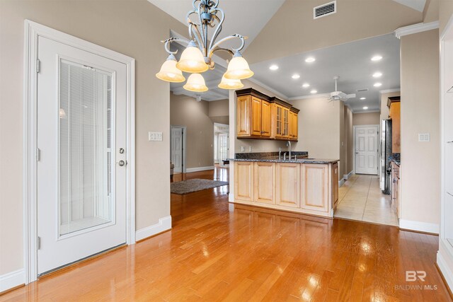 kitchen with pendant lighting, ornamental molding, dark stone counters, stainless steel refrigerator, and light wood-type flooring