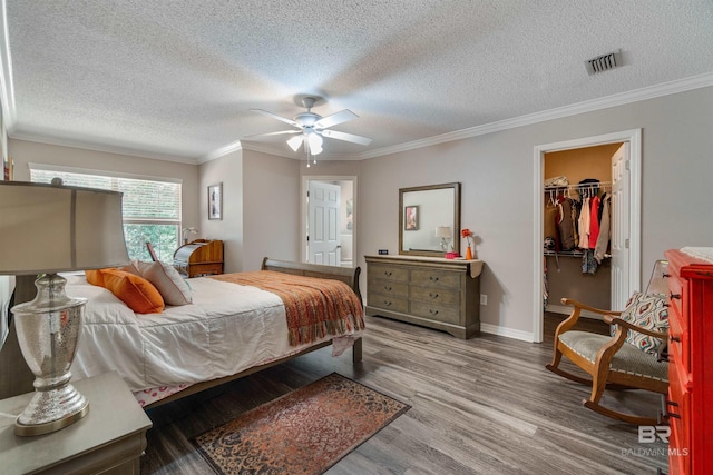 bedroom with hardwood / wood-style flooring, ornamental molding, a spacious closet, and a closet